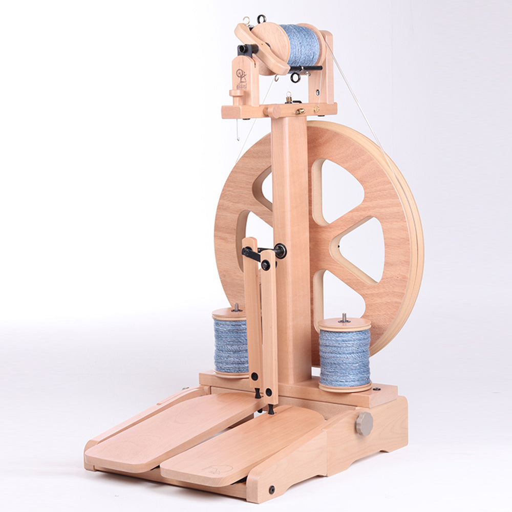 Close-up of the Ashford Kiwi 3 spinning wheel showing the flyer, bobbin, and treadle system on a light wood floor