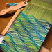 Weaving in progress on a rigid heddle loom using Ashford Caterpillar Yarn in green and blue shades.