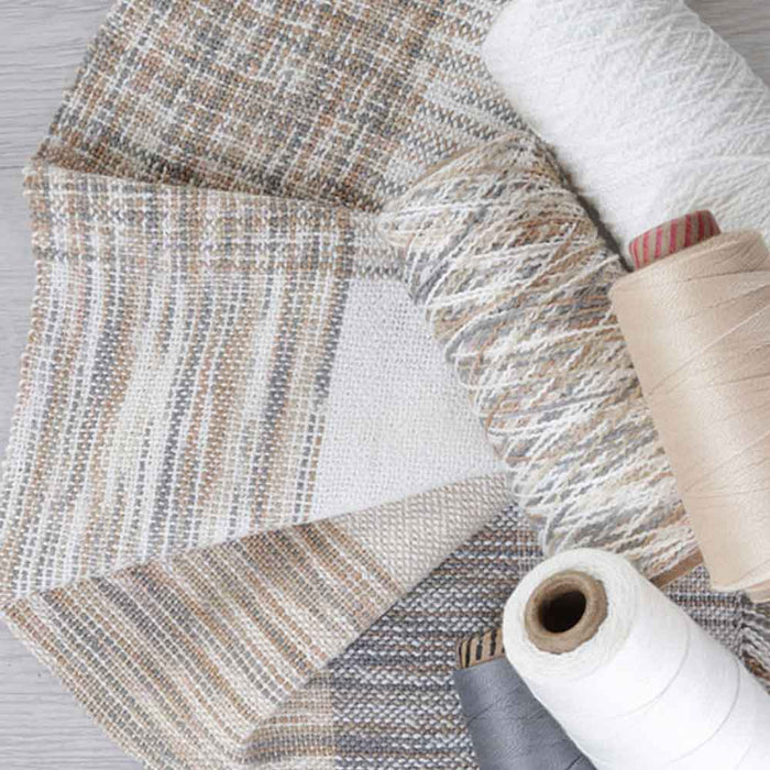 Woven fabric samples made with Ashford Caterpillar Yarn in neutral tones with cones of coordinating yarns.