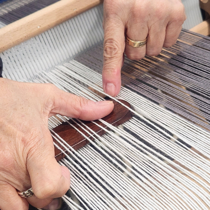 Hands demonstrating pickup stick techniques on a rigid heddle loom