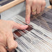 Hands demonstrating pickup stick techniques on a rigid heddle loom