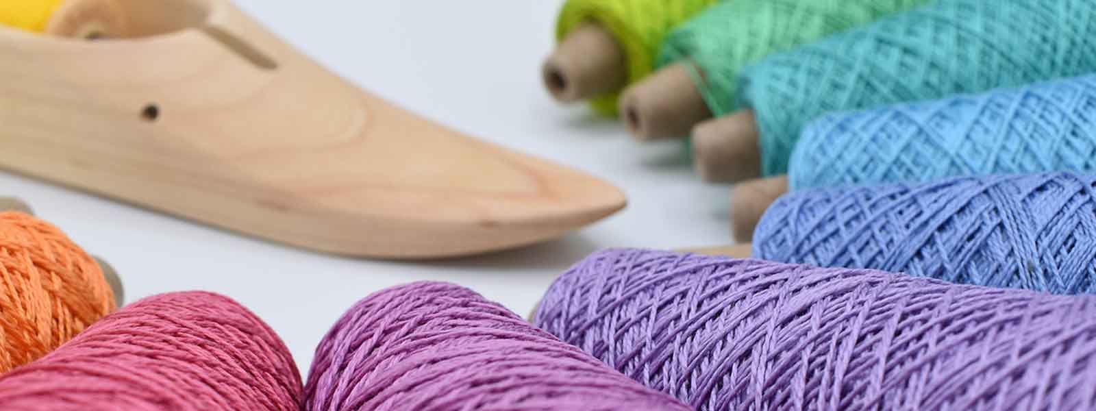Colorful weaving yarn cones arranged beside a wooden weaving shuttle on a white background