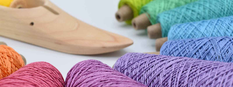 Colorful weaving yarn cones arranged beside a wooden weaving shuttle on a white background